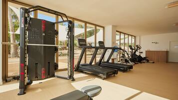 Un gimnasio con equipo de ejercicio, incluyendo cintas de correr y una máquina de pesas, con ventanas amplias que ofrecen vistas al exterior.