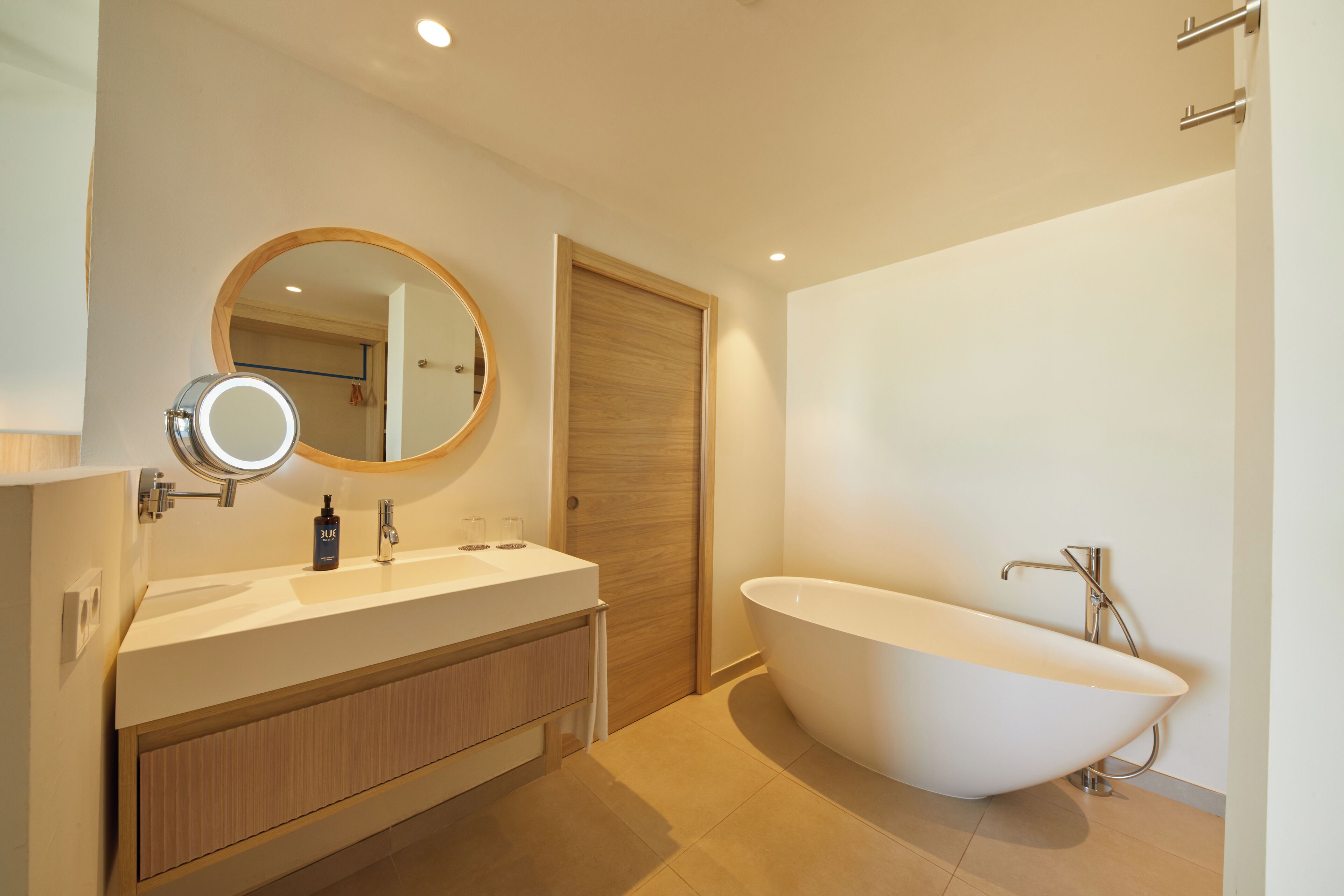 Un baño moderno con una bañera independiente, un espejo redondo y un tocador de madera.
