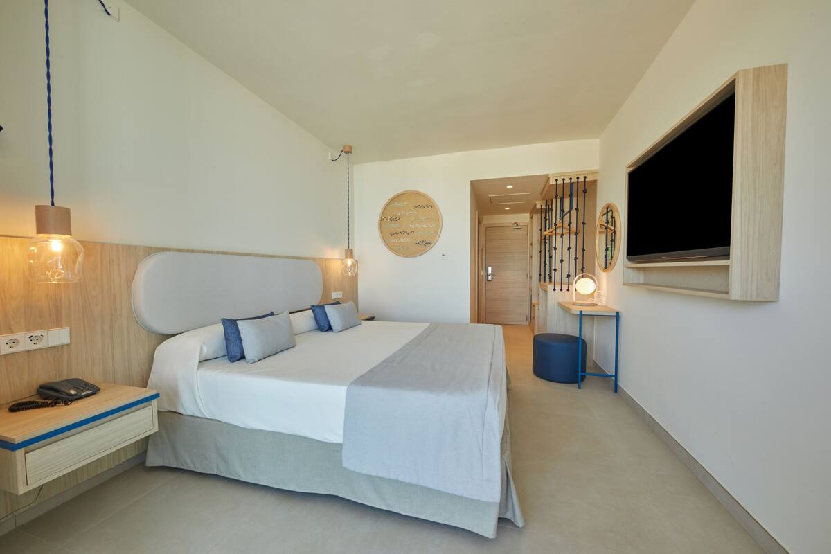 Un dormitorio moderno con una cama grande, mesita de noche, lámpara y televisión montada en la pared.