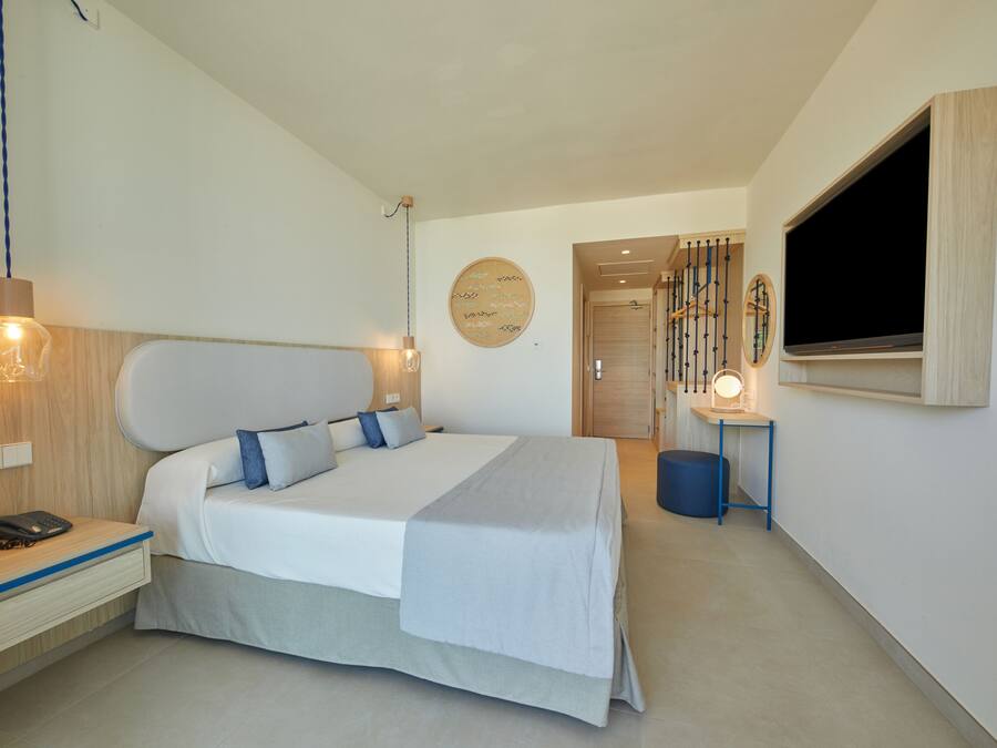 Un dormitorio moderno con una cama grande, mesita de noche, lámpara y televisión montada en la pared.