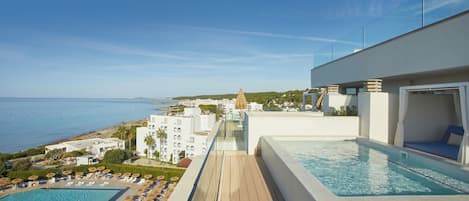 A rooftop pool area with a view of the sea, a lounge with a pool, and a clear sky.