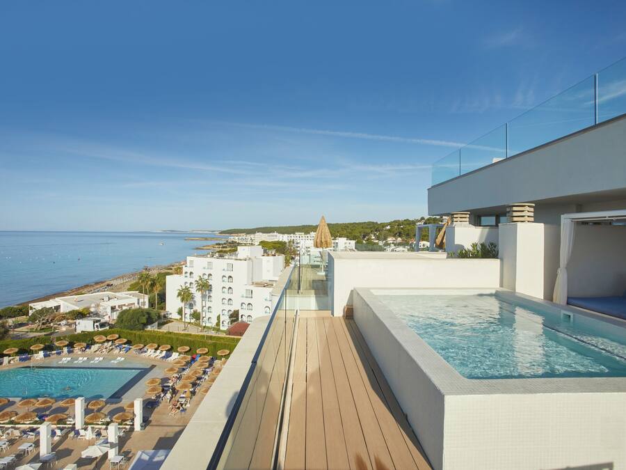 A rooftop pool area with a view of the sea, a lounge with a pool, and a clear sky.