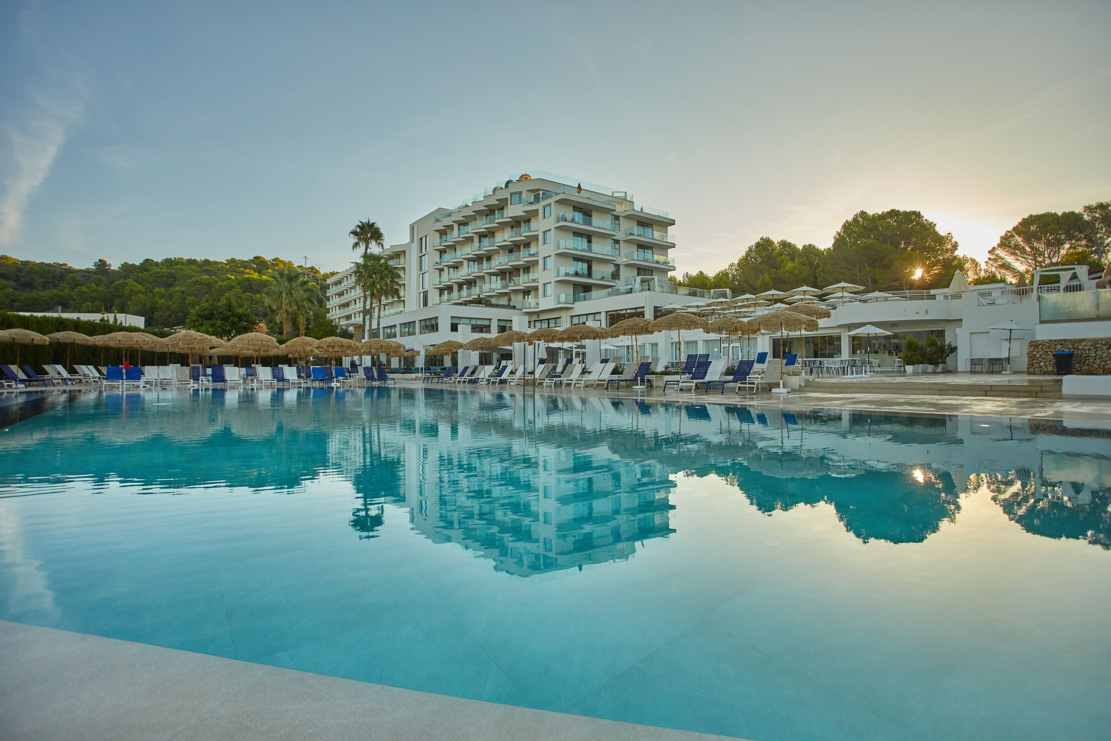A hotel with a swimming pool, sun loungers, and umbrellas.
