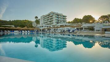 A hotel with a swimming pool, sun loungers, and umbrellas.
