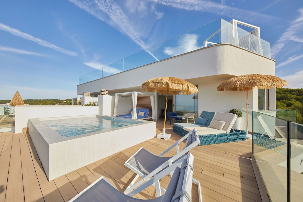 Un área de piscina moderna en la azotea, con barandilla de vidrio, sillas de descanso y un jacuzzi.