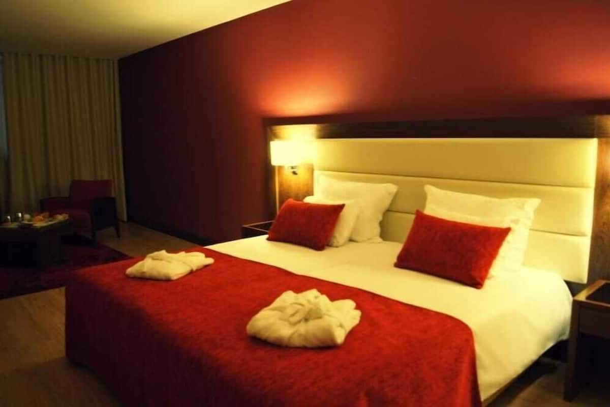 Une chambre d’hôtel avec un grand lit, une literie rouge et blanche, une tête de lit en bois et une lampe de chevet.