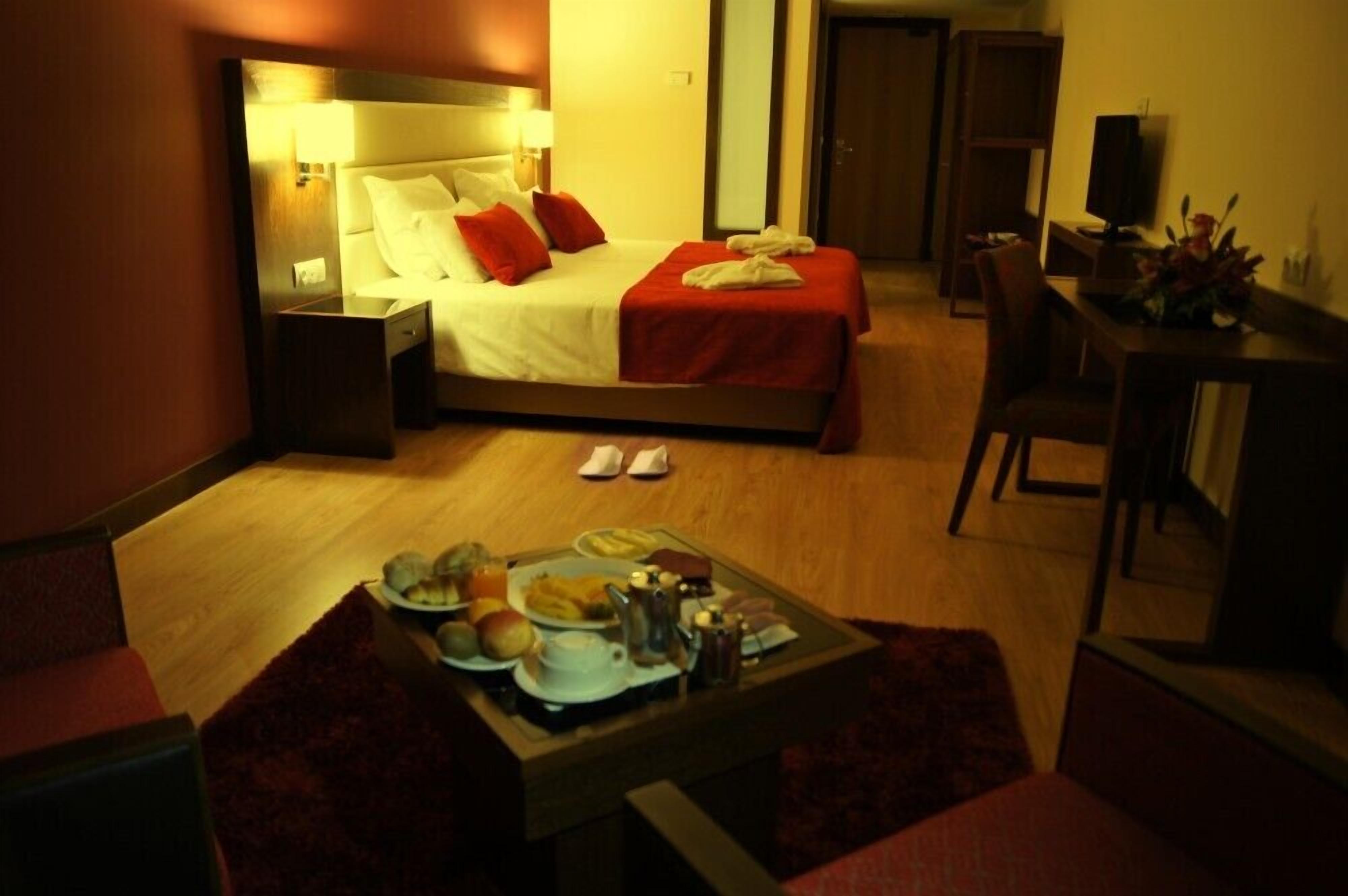 Una habitación de hotel con cama, mesita de noche y una bandeja de desayuno sobre una pequeña mesa.
