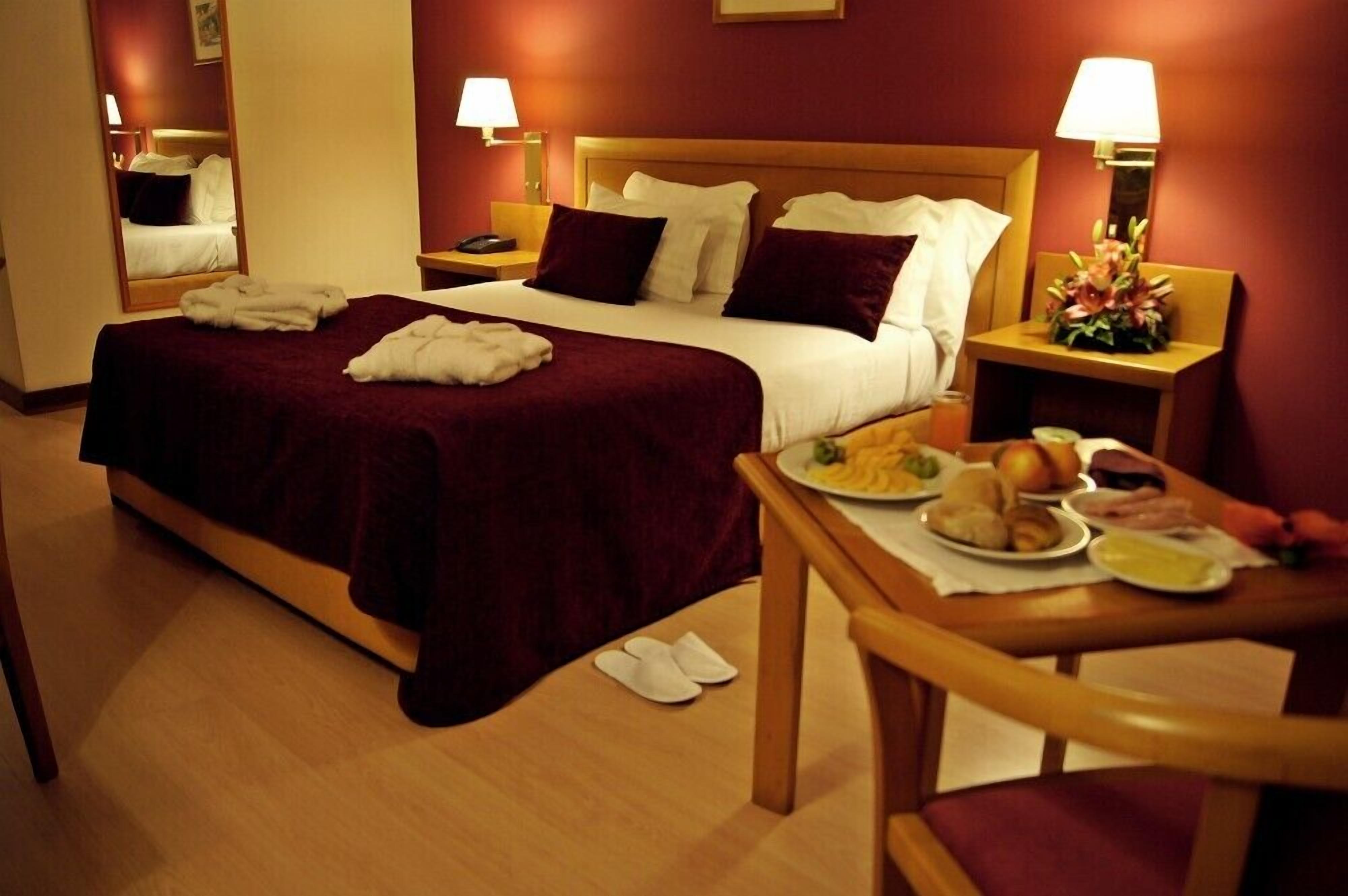 Habitació d'hotel amb un llit, taules de nit, una cadira i un carret de servei d'esmorzar.