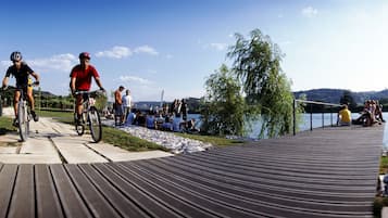 Un paseo marítimo de madera junto a un lago, con gente andando en bicicleta y sentada.