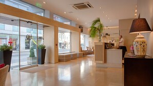 A hotel lobby with a reception desk, seating area, and large windows offering views of the street. - Hotel Oslo (Coimbra)