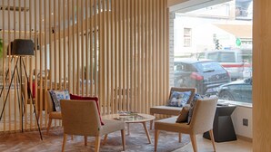 A modern interior with a seating area featuring two sofas and a coffee table, a floor lamp, and a view of the street through large windows. - Hotel Oslo (Coimbra)