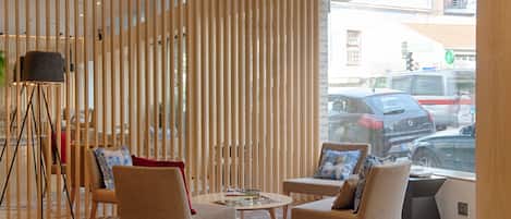 A modern interior with a seating area featuring two sofas and a coffee table, a floor lamp, and a view of the street through large windows.