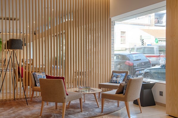 Un interior moderno con una zona de estar que incluye dos sofás, una mesa de centro, una lámpara de pie y vistas a la calle a través de amplios ventanales.