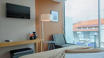 Habitación de hotel con cama, escritorio con lámpara, silla y televisor montado en la pared.