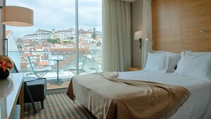A hotel room with a large bed, a desk with a lamp, and a view of a cityscape through large windows. - Hotel Oslo (Coimbra)