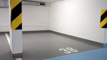 Un estacionamiento con paredes blancas, columnas rayadas de negro y amarillo, y un piso azul con el número 38 pintado.