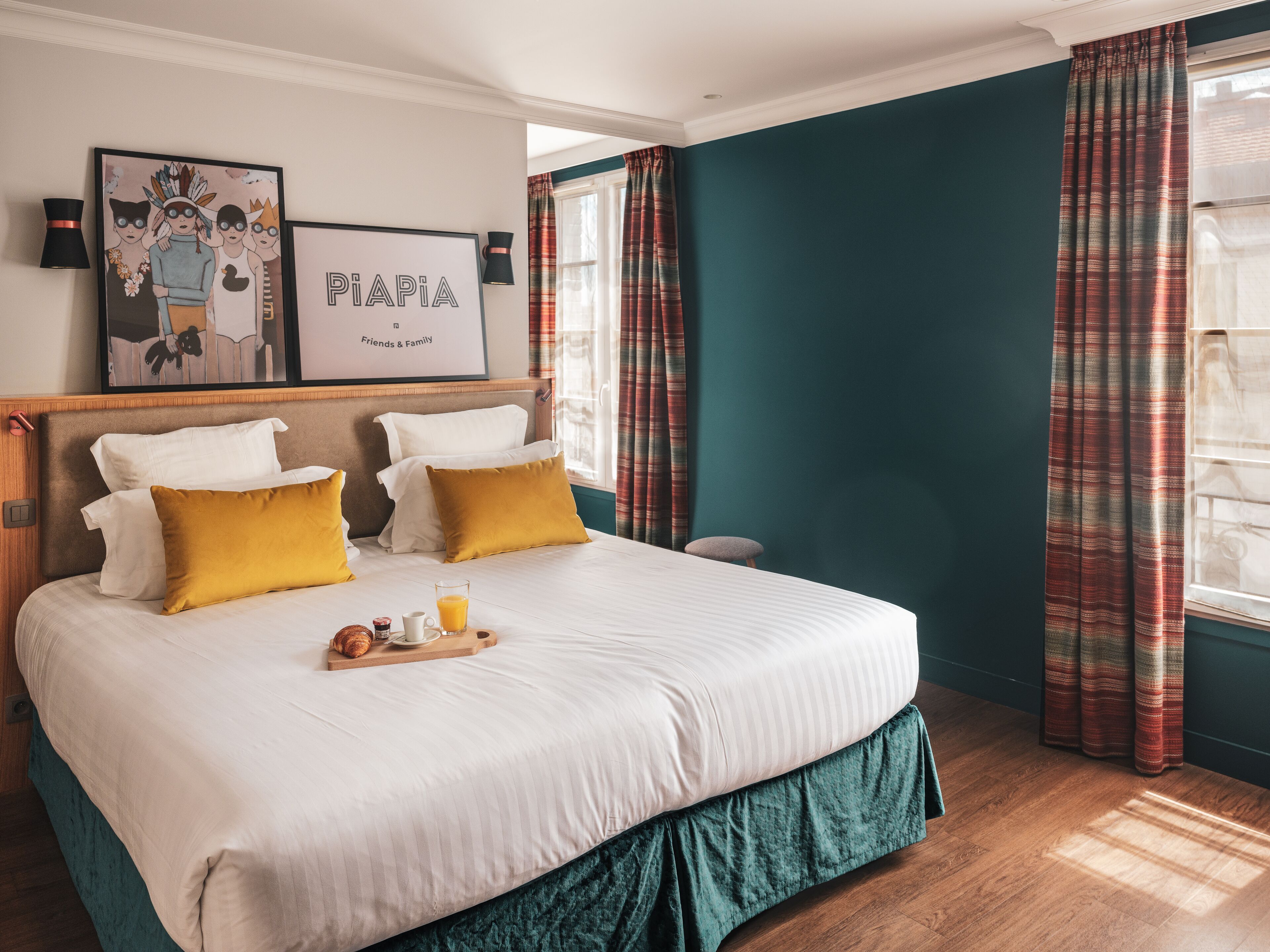 A neatly made bed with white and mustard pillows, a tray with croissants, and a framed artwork above it.