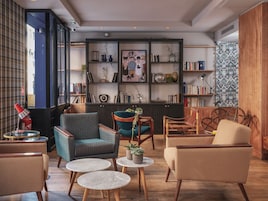 A cozy lounge area with comfortable seating, a bookshelf with various items, and a view through a window.
