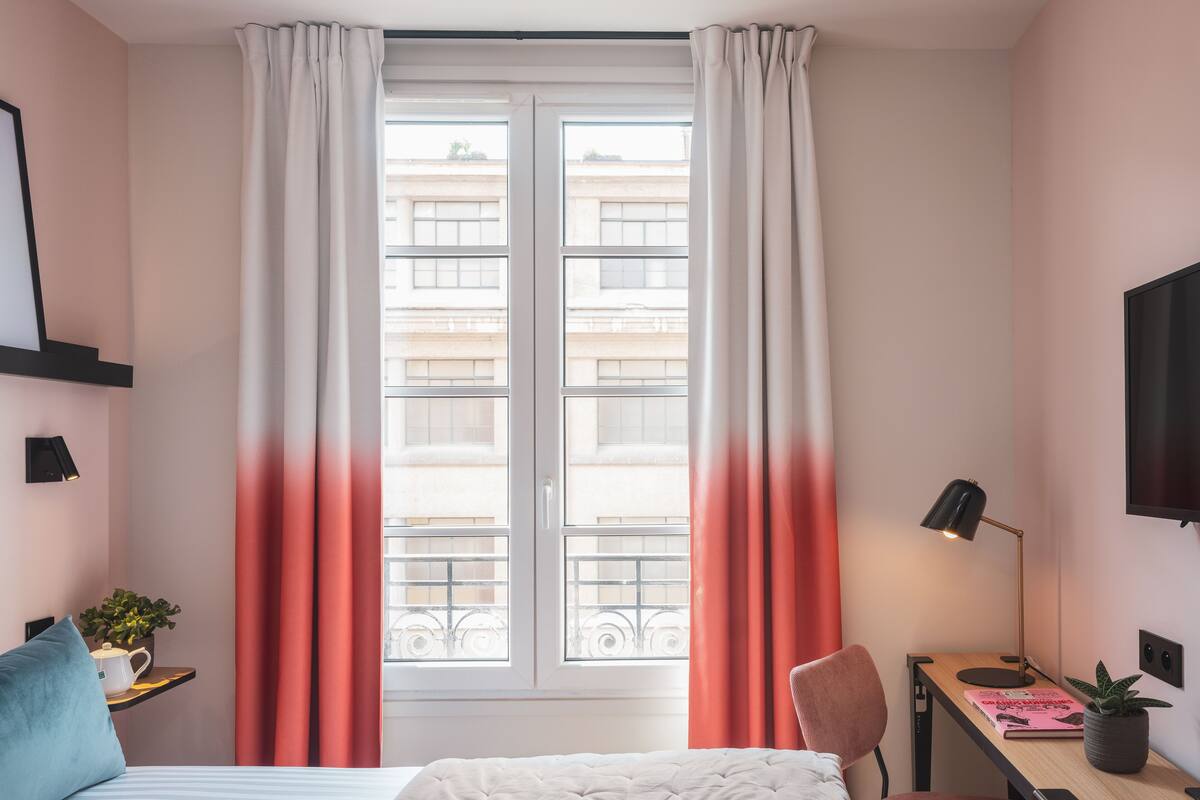Une chambre à coucher avec un lit, un bureau, une chaise, une télévision et une fenêtre avec des rideaux.