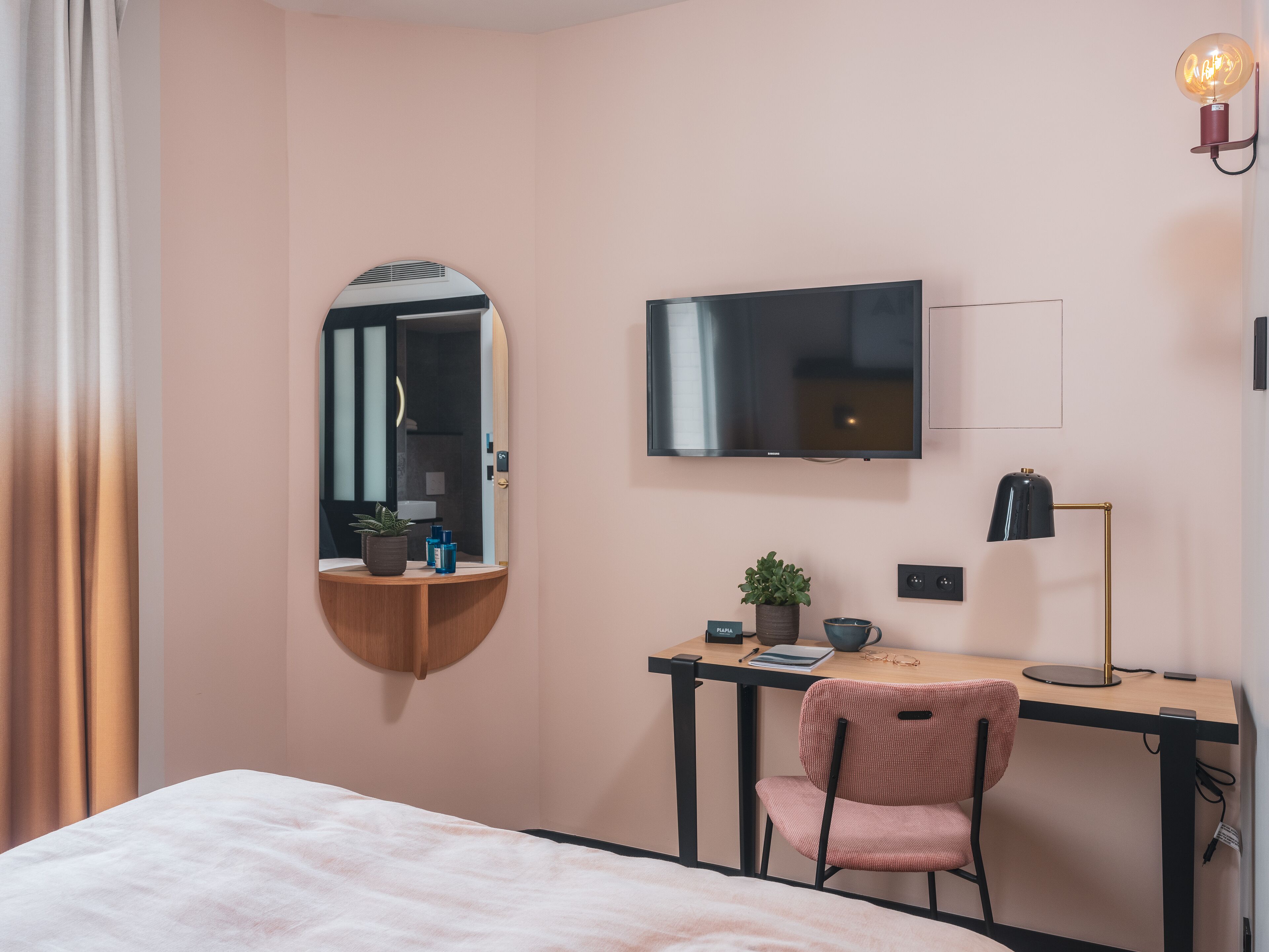 Habitación de hotel con cama, escritorio, silla, televisión, espejo y lámpara.