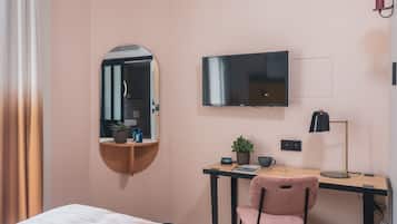 Ein Hotelzimmer mit einem Bett, einem Schreibtisch mit Stuhl, einem Fernseher, einem Spiegel und einer Lampe.
