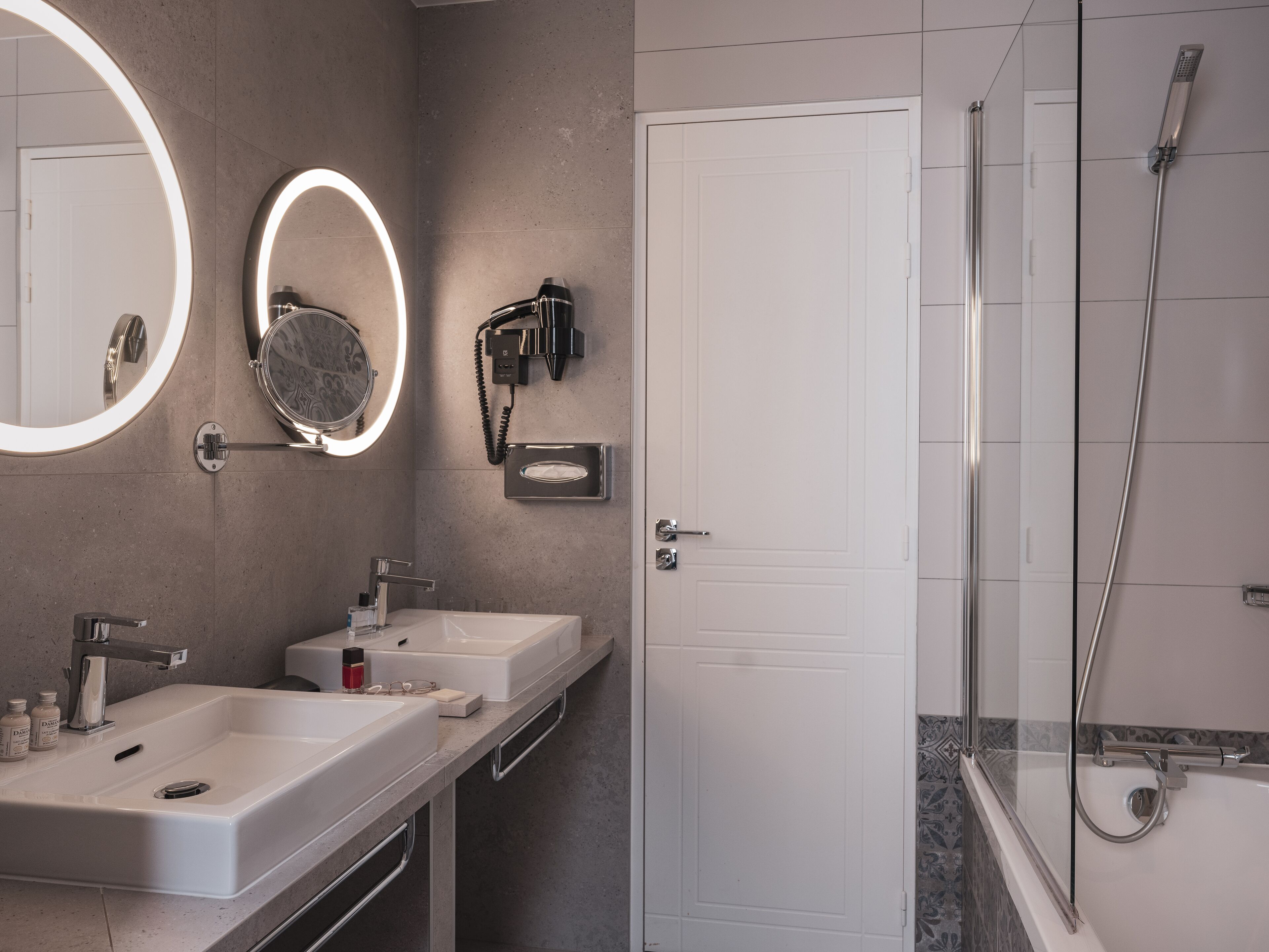 Un bagno moderno con due lavabi, uno specchio grande con illuminazione e un asciugacapelli, oltre a una zona doccia.