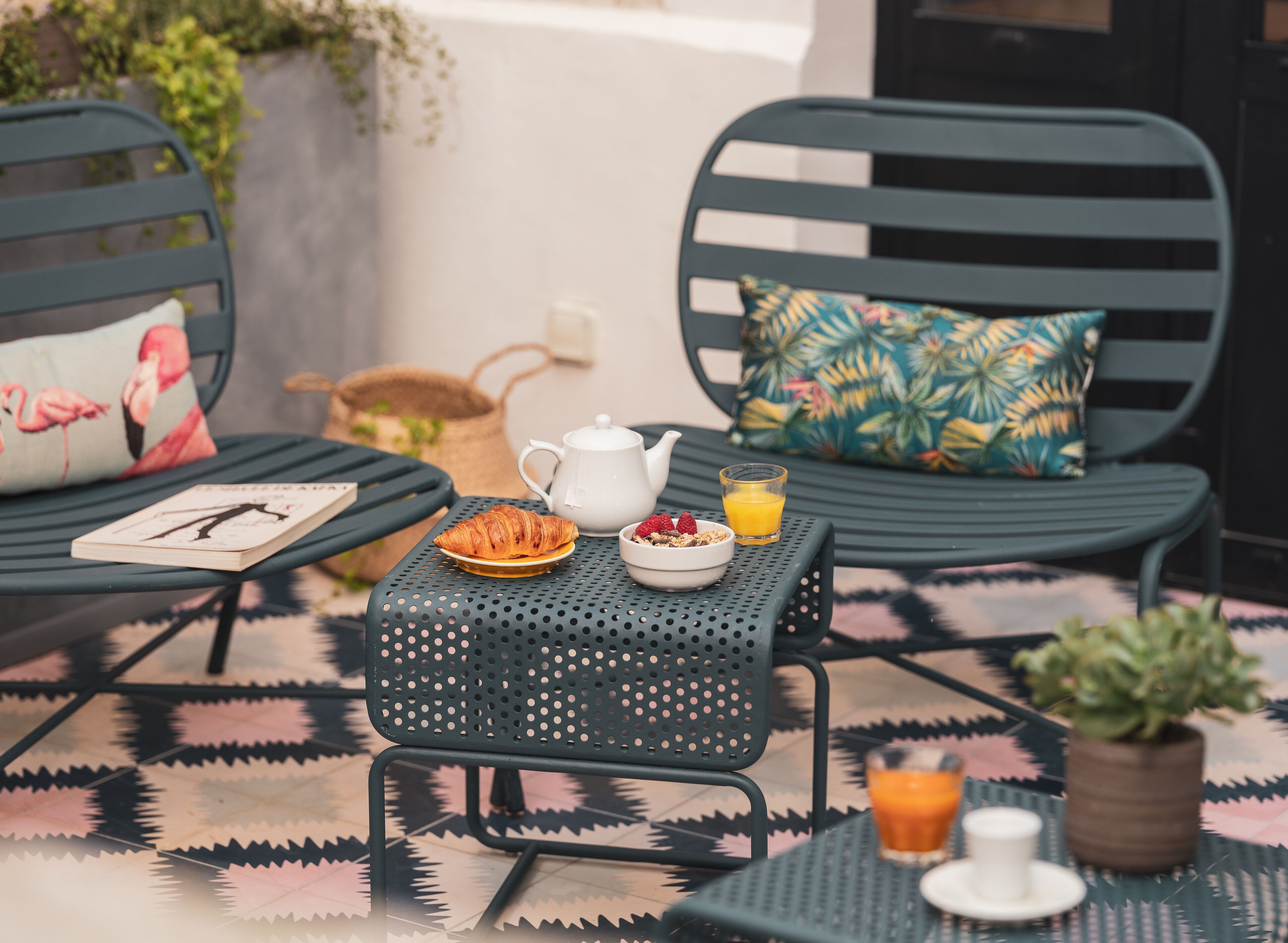 A dining area with a table set for breakfast, including croissants, a teapot, and a glass of orange juice.