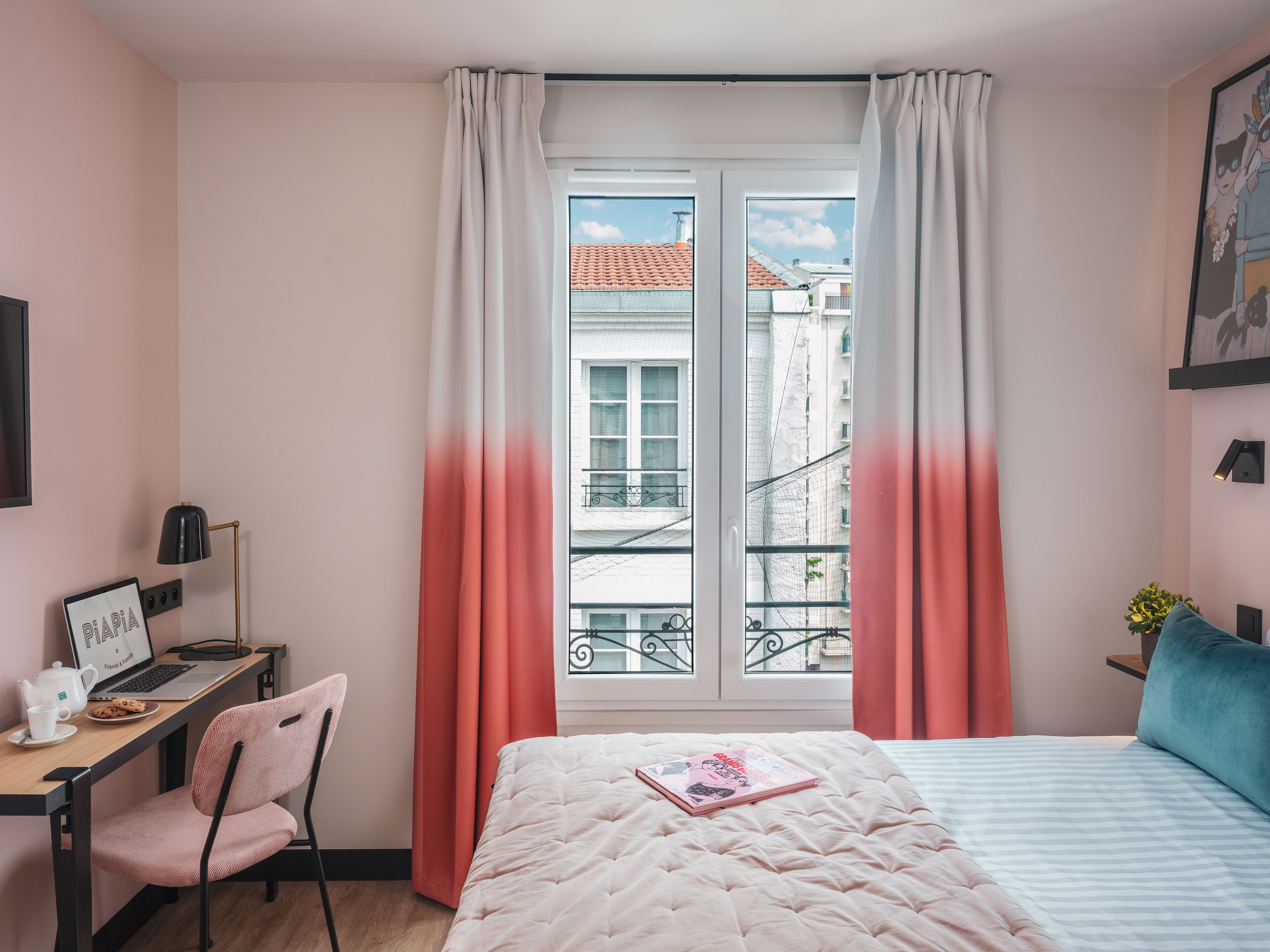 A bedroom with a bed, a desk with a laptop, a chair, and a window with curtains.