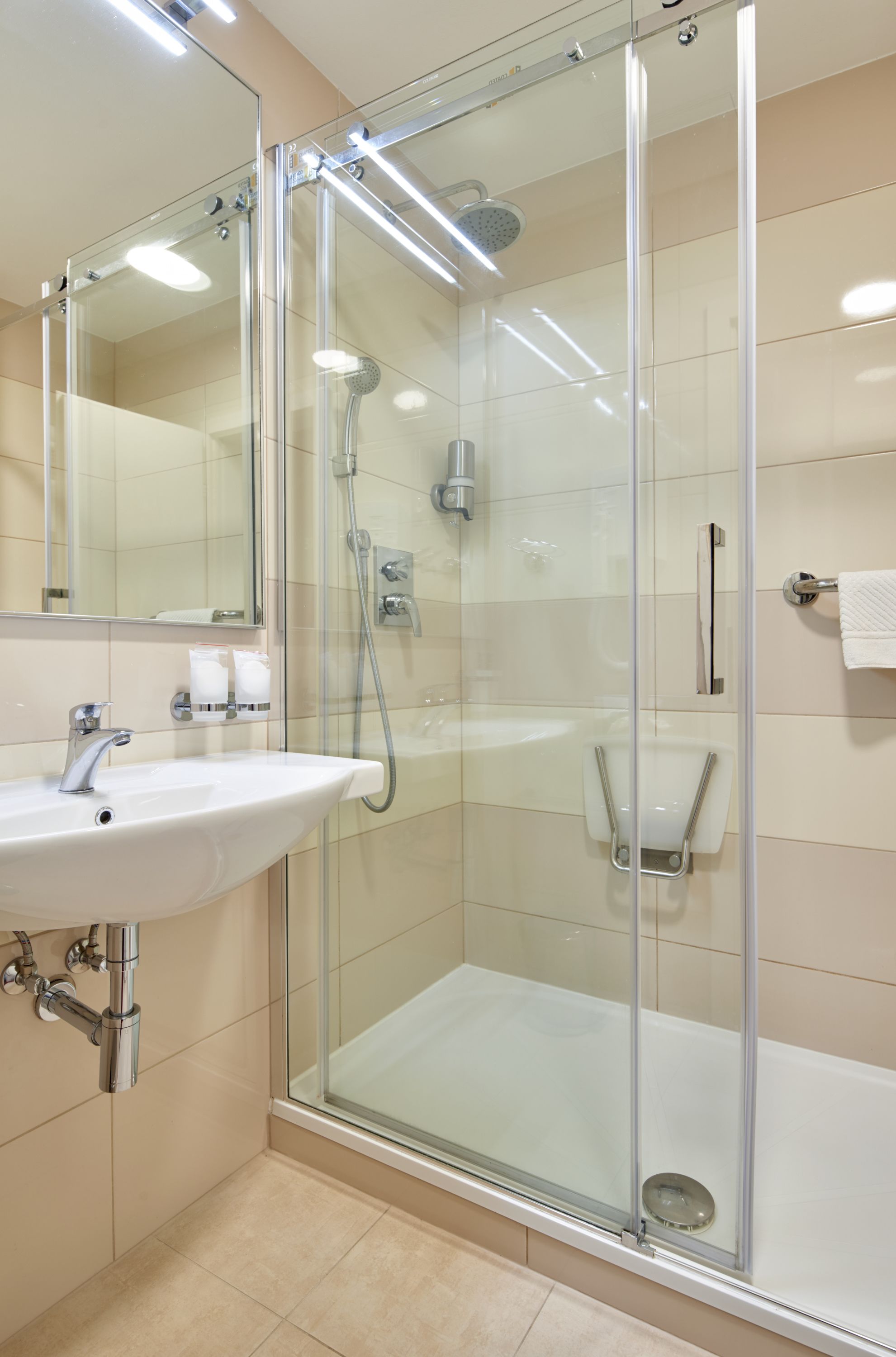 Un bany modern amb dutxa de vidre, un lavabo blanc i un mirall.