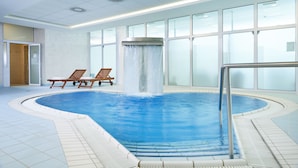 Una piscina interior con cascada, sillones reclinables y grandes ventanales.