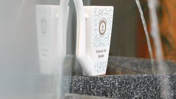 Una fuente de agua con cerramiento de vidrio, una jarra de cerámica blanca y un caño.