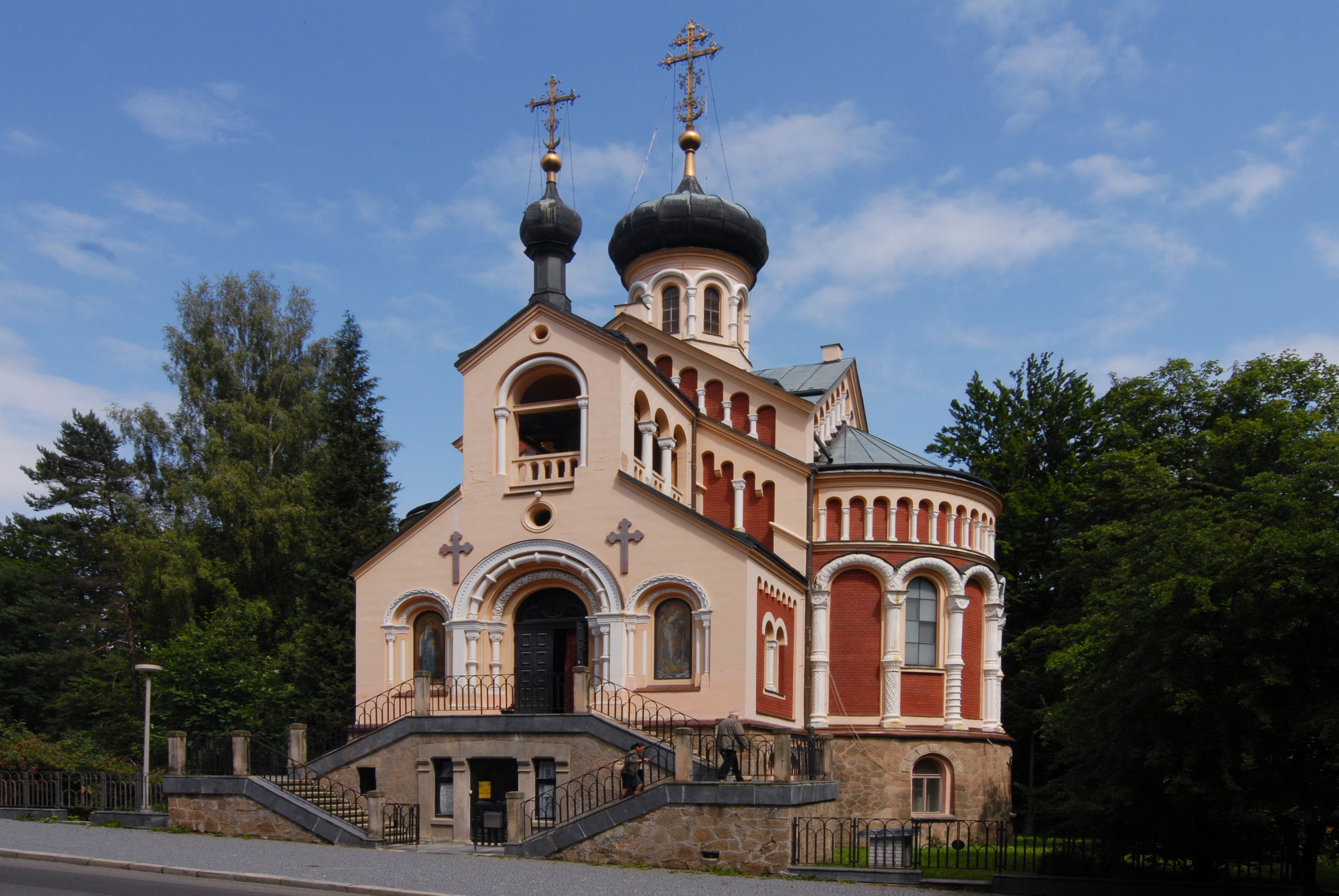 A church with a prominent dome and two crosses on top, surrounded by trees.