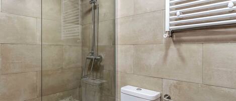 A bathroom with a glass-enclosed shower, a toilet, and a towel rack.