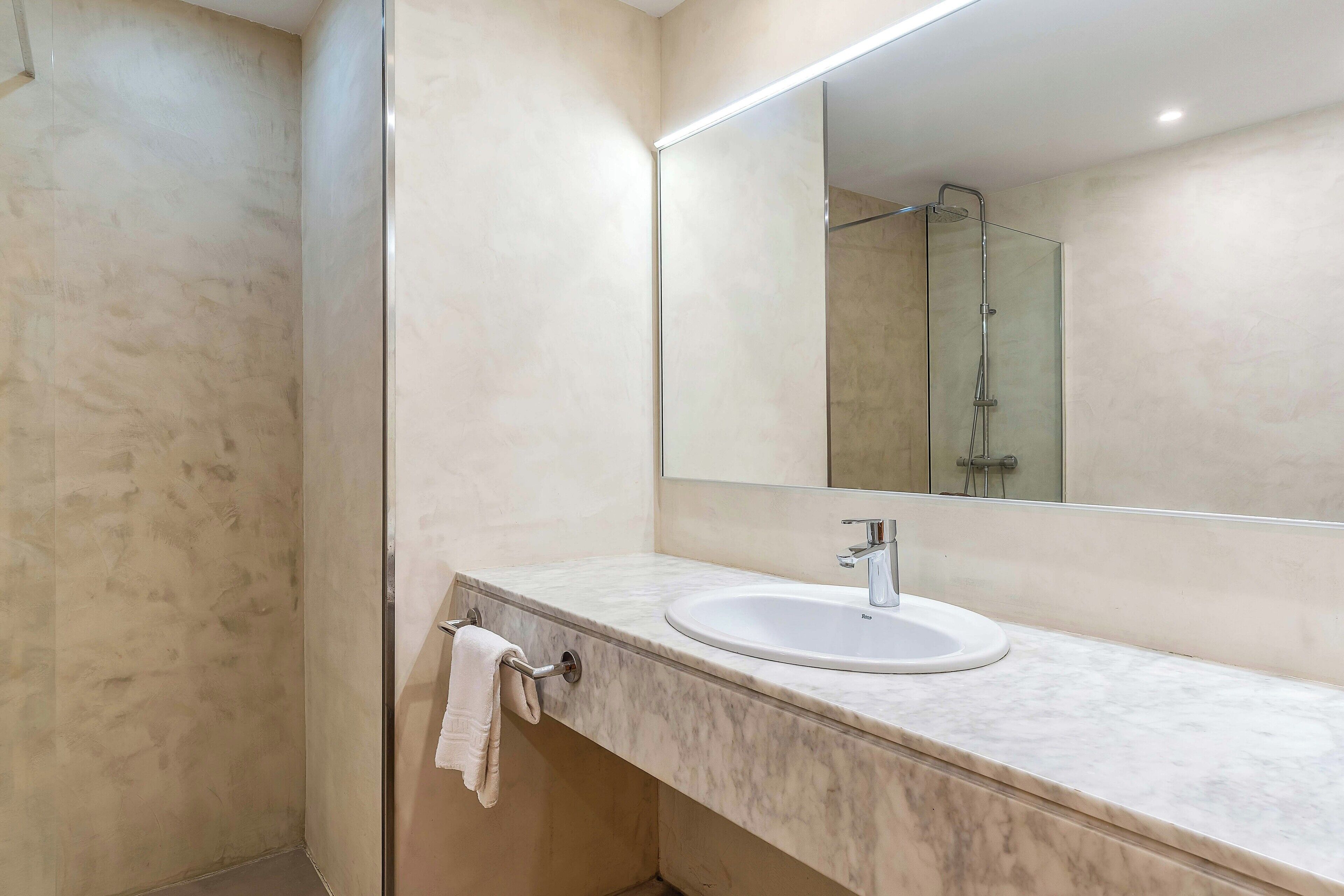 Een moderne badkamer met een marmeren wastafel, een grote spiegel en een douchecabine van glas.