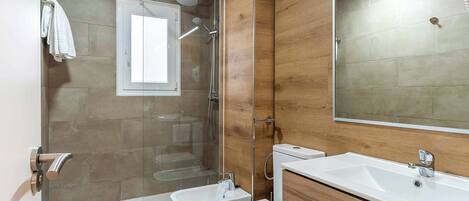 A modern bathroom with a shower, bidet, toilet, and a large mirror.