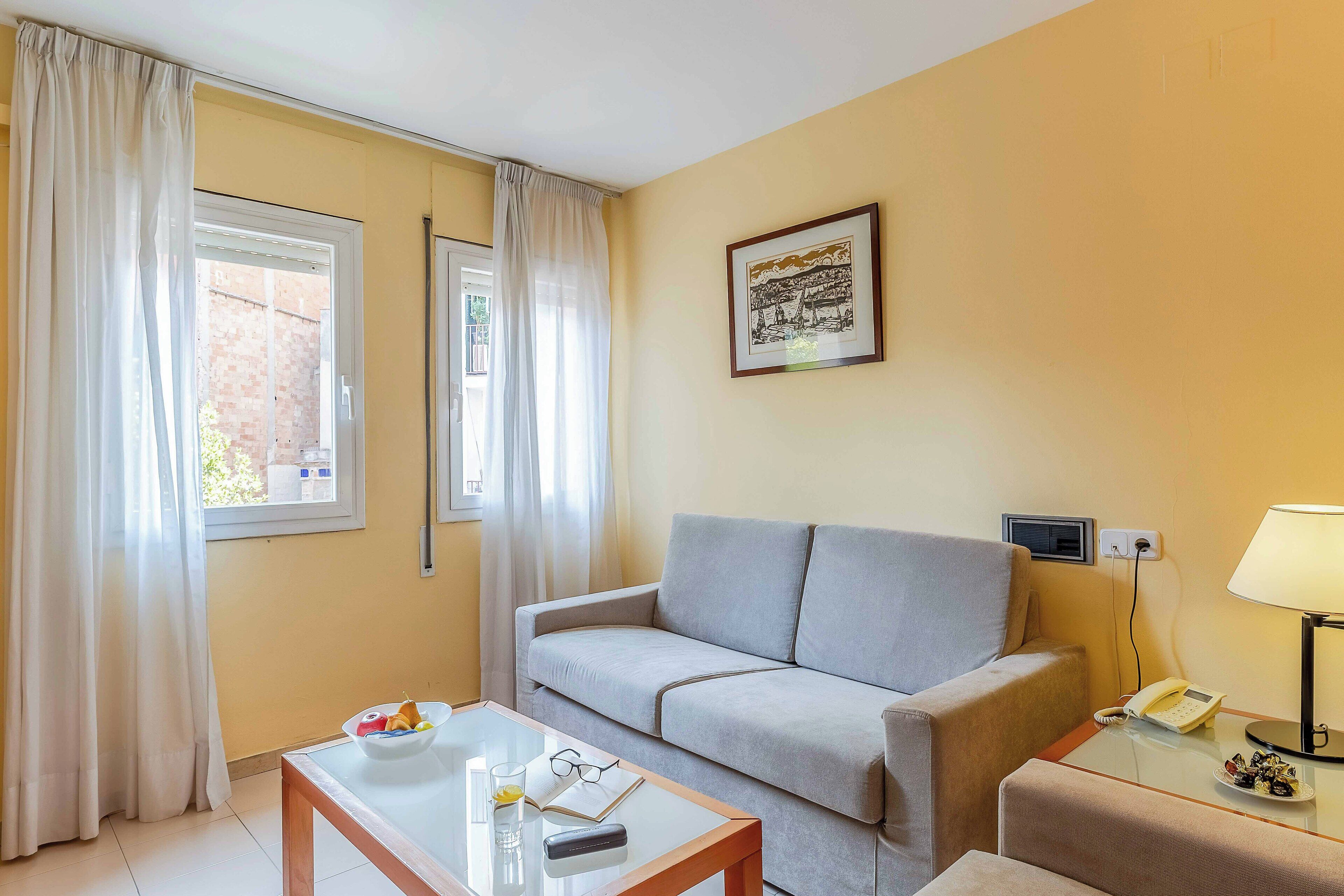 Een kamer met een bank, een glazen tafel met een schaal, een lamp en een ingelijst schilderij aan de muur.