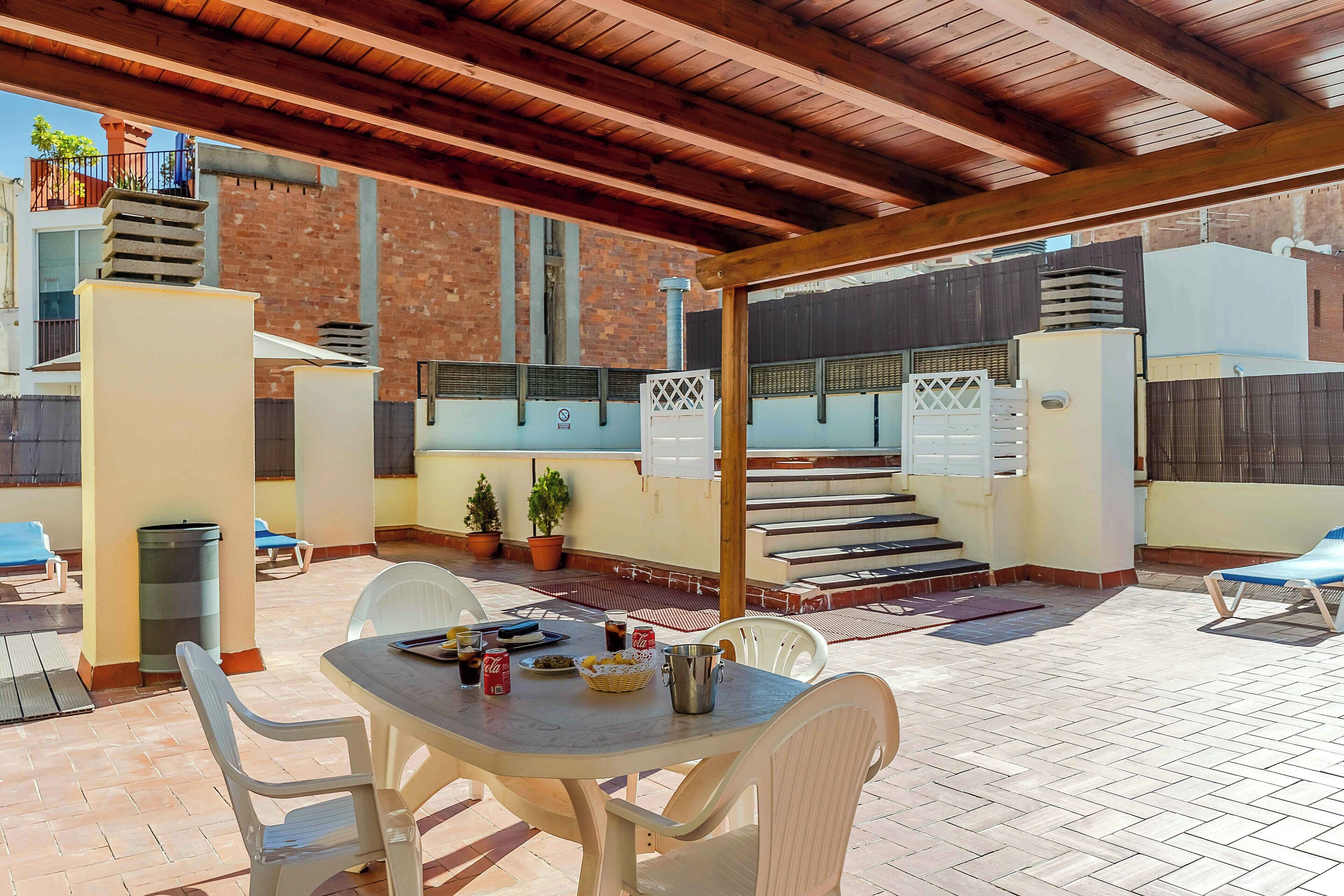An outdoor patio area with a covered seating area, a table with drinks, and potted plants.