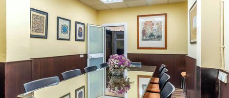 A conference room with a glass table, black chairs, framed artwork on the walls, and a door labeled "SALA DE CONFERENCIA".