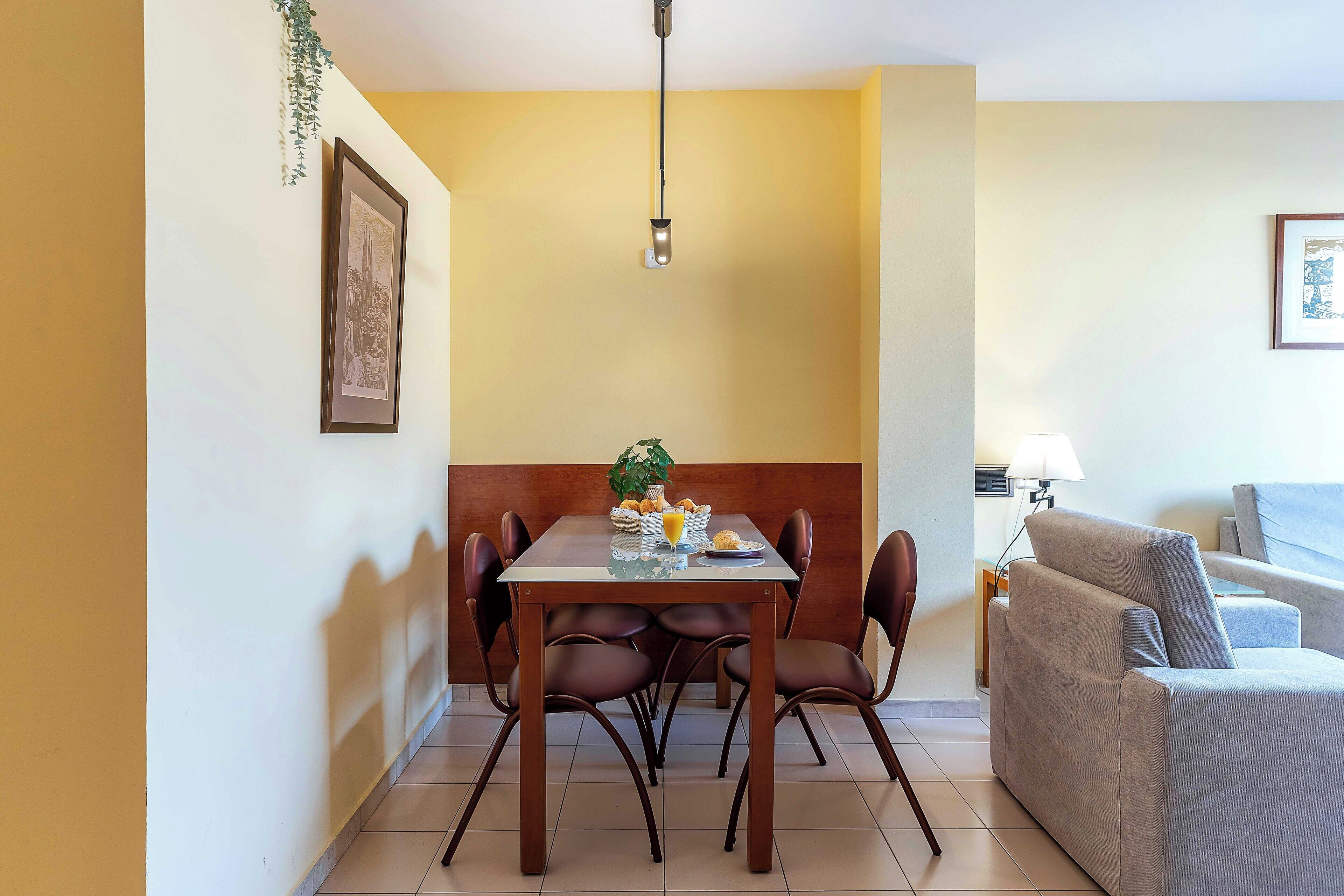 Uma área de refeições com uma mesa, cadeiras, uma planta pendente e um quadro na parede.