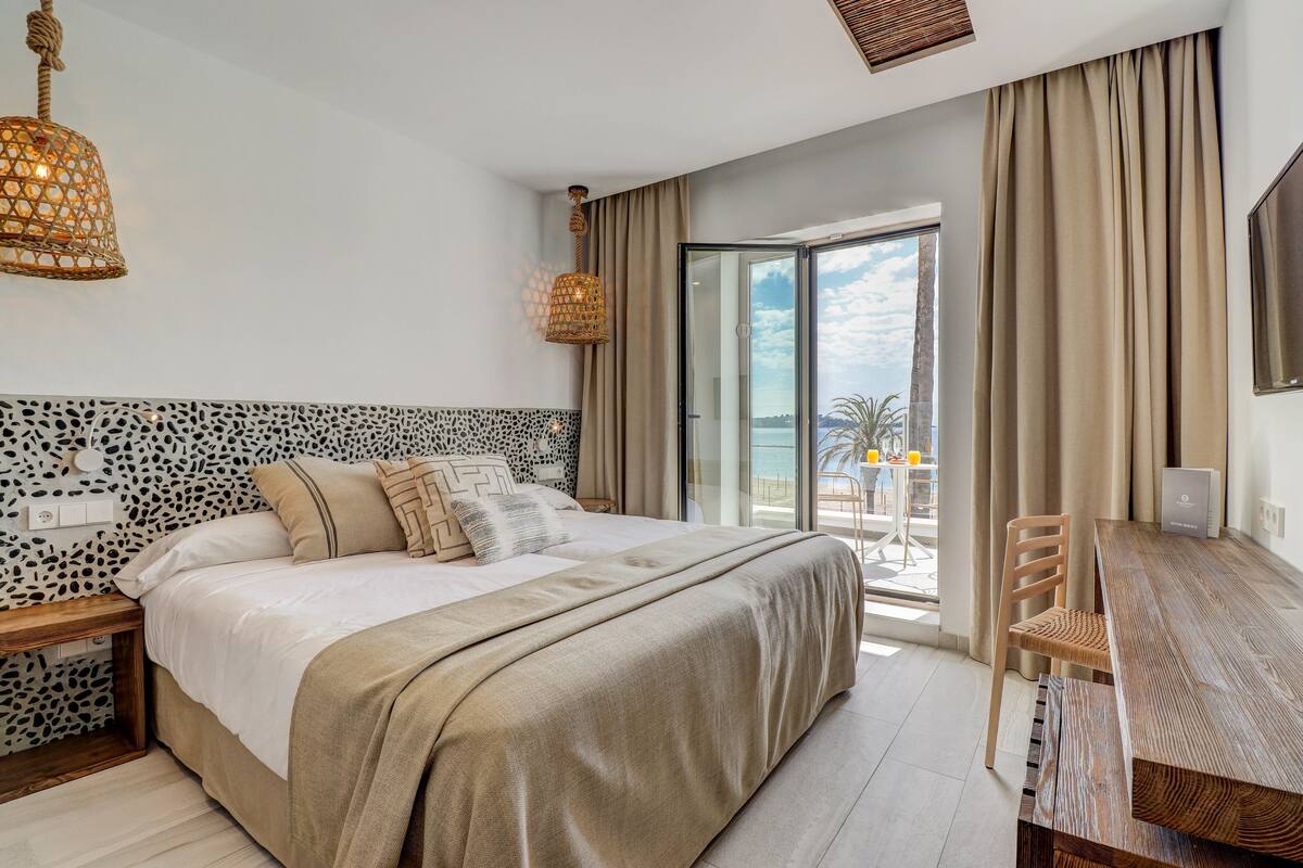 A modern bedroom with a large bed, a wooden desk, and a view of the outdoors.