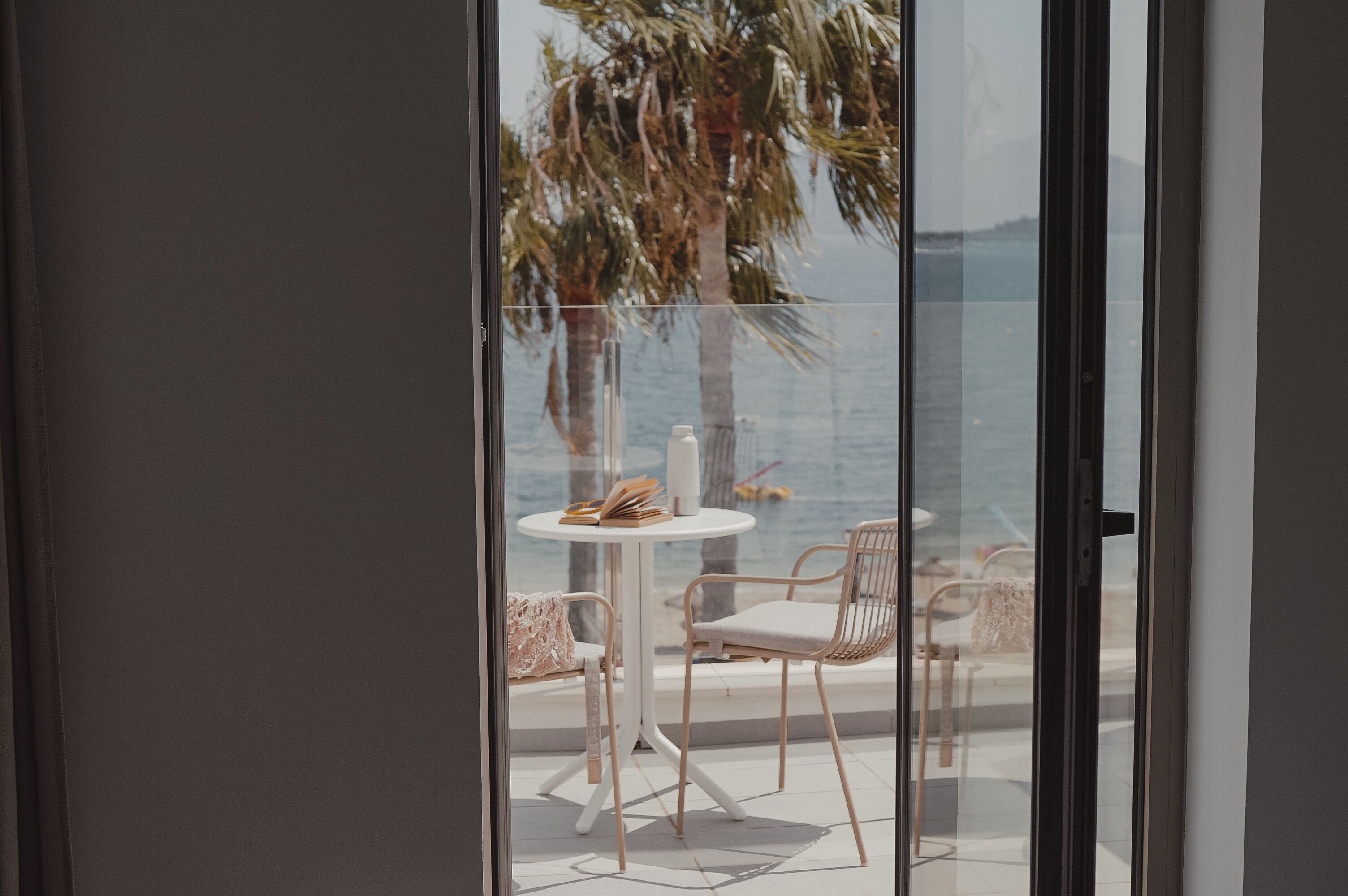 Ein Balkon mit einem weißen Tisch und zwei Stühlen mit Blick auf ein Gewässer und Palmen.
