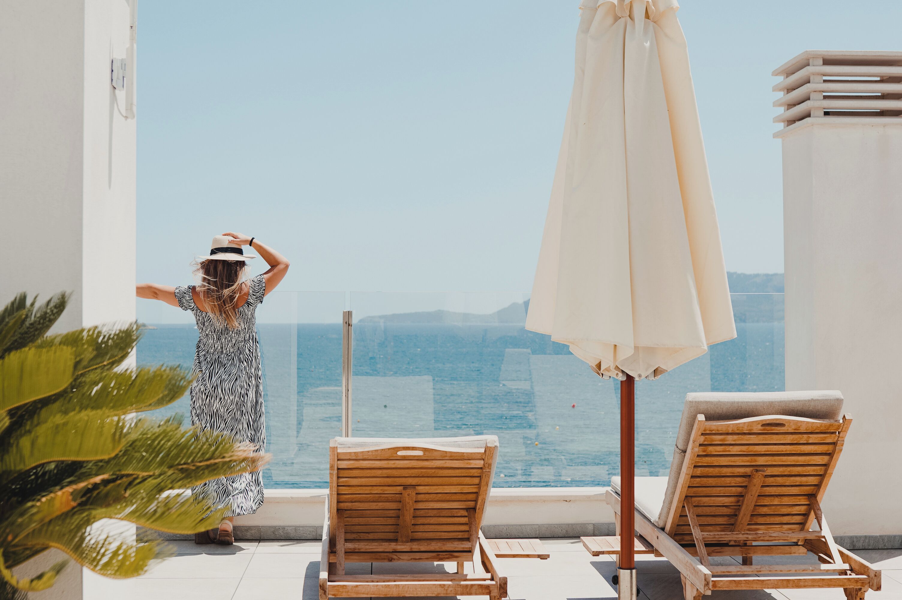 Un balcó amb vista al mar, dues cadires de relax de fusta i un parasol gran.