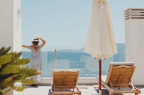 Un balcon avec vue sur la mer, deux fauteuils de jardin en bois et un grand parasol.