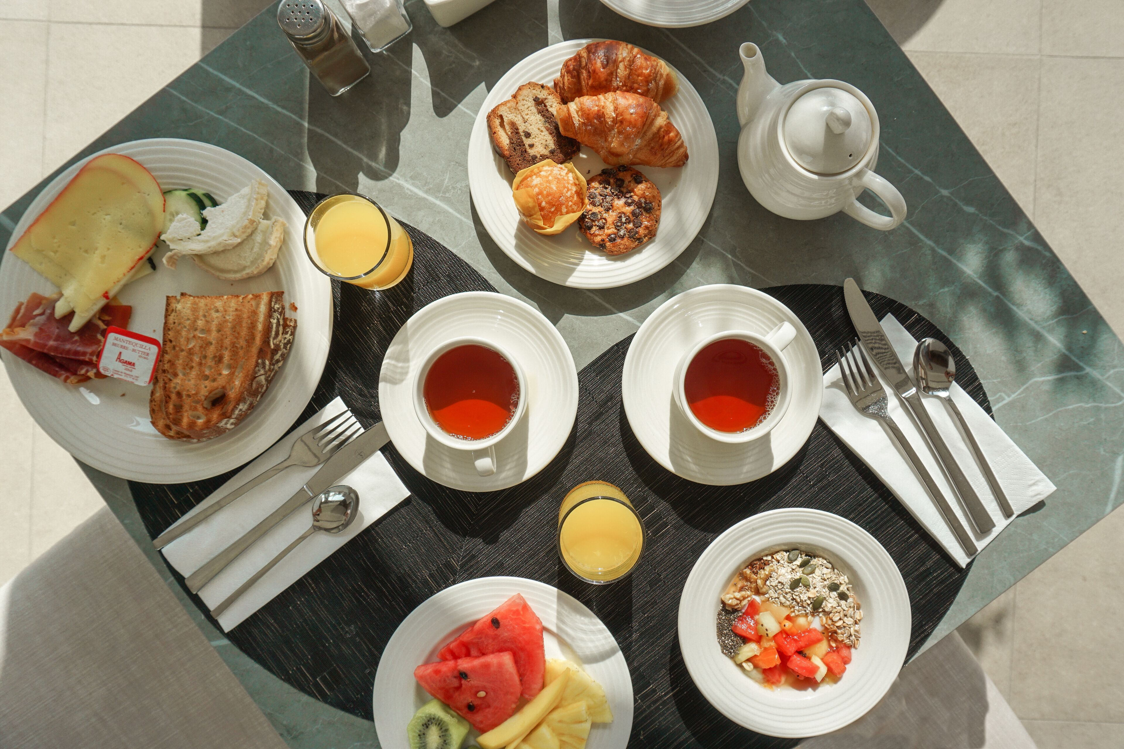 A breakfast setting with croissants, toast, fruit, and beverages on a table.