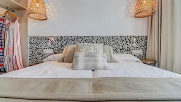 Una cama bien tendida con almohadones estampados, cabecera con diseño geométrico blanco y negro, y dos lámparas colgantes.