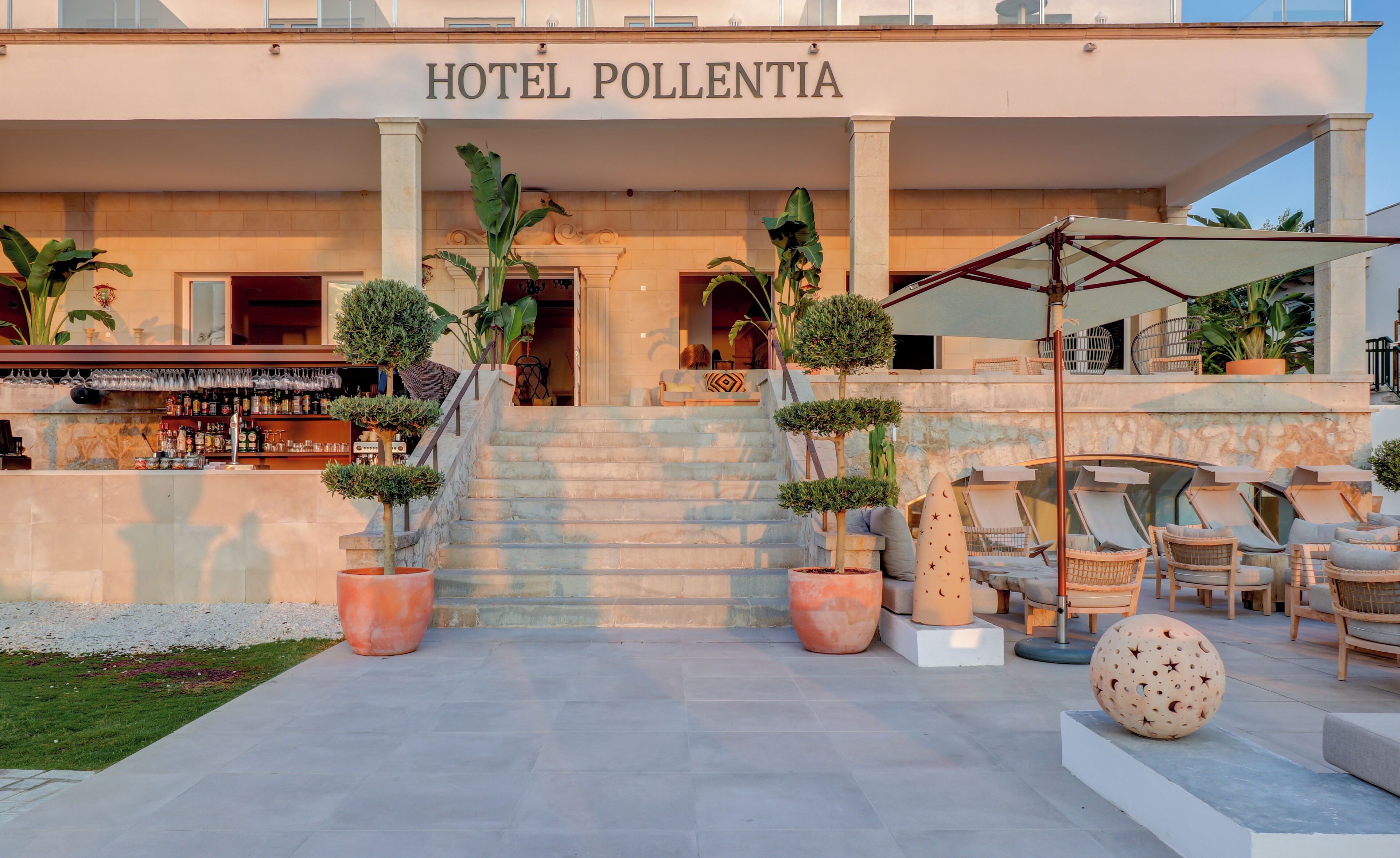 La entrada del HOTEL POLLENTIA con una zona de bar, asientos exteriores y plantas en macetas.