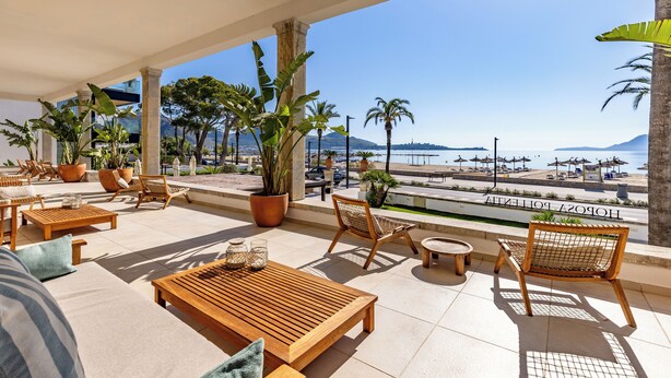 En terrasse med træmøbler, plantekasser og udsigt til strand og hav.