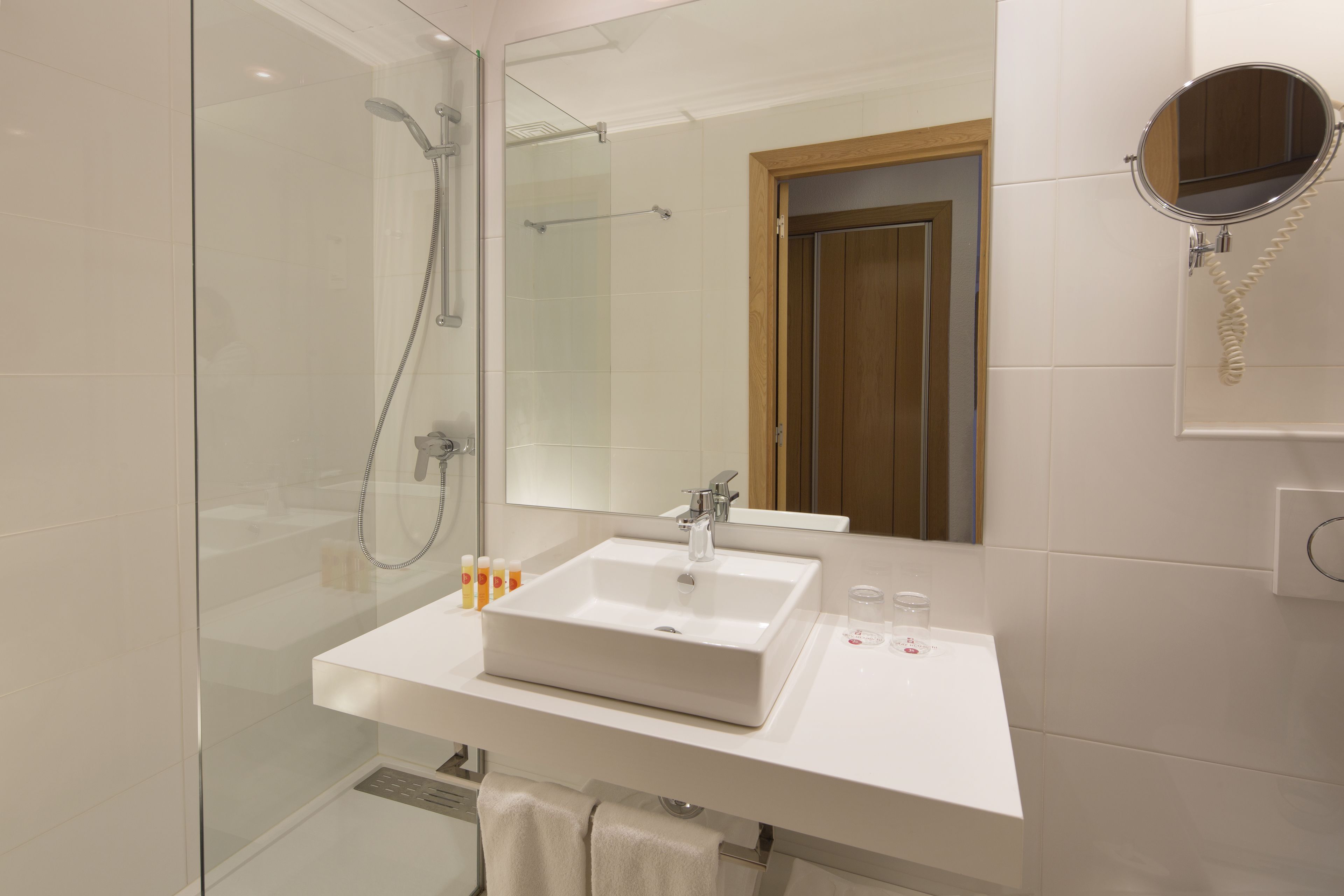 A modern bathroom with a glass-enclosed shower, a white sink, and a mirror with a telephone.