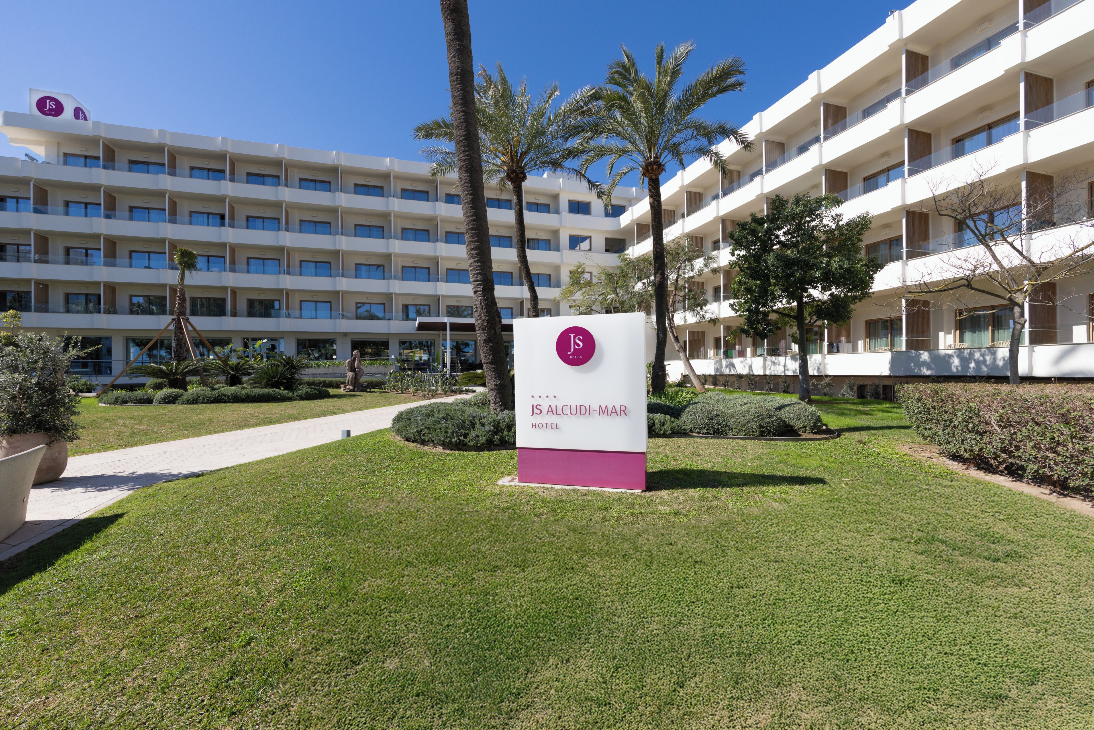 Un letrero de hotel que dice 'JS ALCUDI-MAR HOTEL' y un edificio con varios balcones y ventanas.