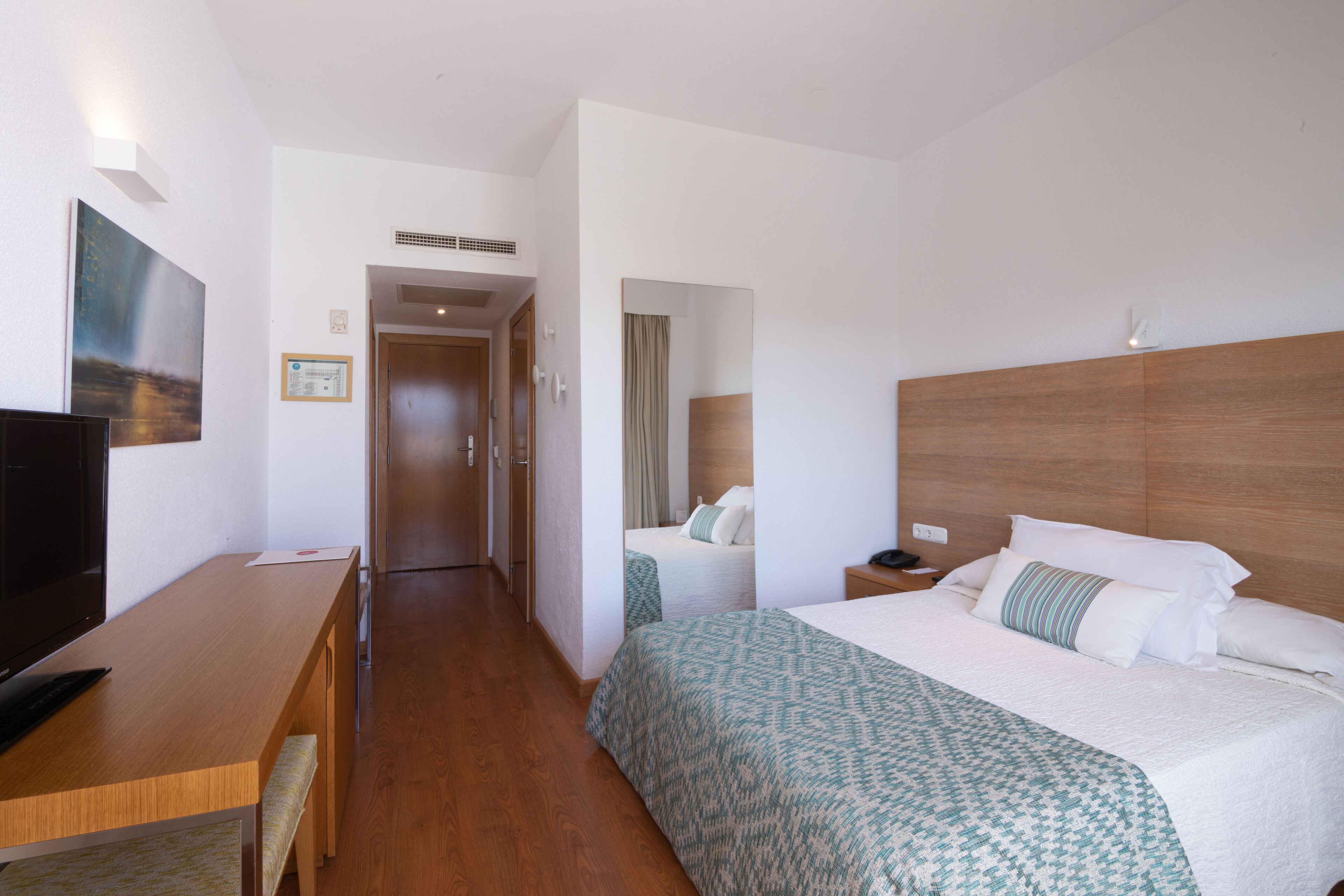 Ein Hotelzimmer mit Holztisch, einem Bett mit gemusterten Betttextilien, einem Fernseher und einem Spiegel.